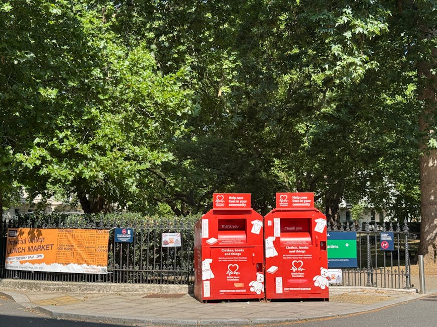 A large green clothing donation bin with Chinese characters and contact information printed on it, situated outdoors against a background of trees and foliage. The bin has multiple compartments for di